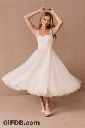 A Woman In A White Dress Is Smiling And Dancing GIF