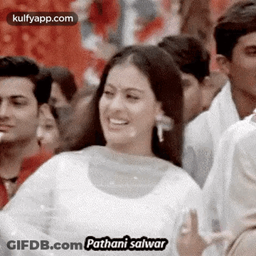 A Woman In A White Dress Is Smiling In Front Of A Crowd . GIF