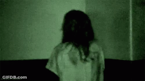 A Woman In A White Dress Is Standing In A Dark Room With A Green Light Behind Her . GIF