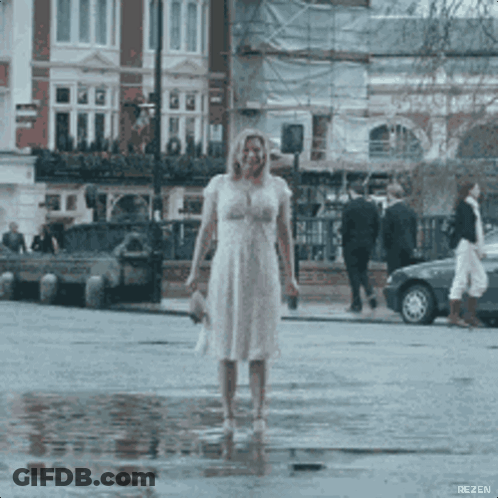 A Woman In A White Dress Is Standing In A Puddle Of Water .. GIF