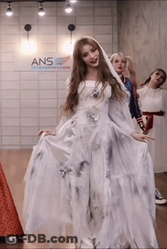 A Woman In A White Dress Is Standing In A Room With Other Women Dressed In Costumes . GIF