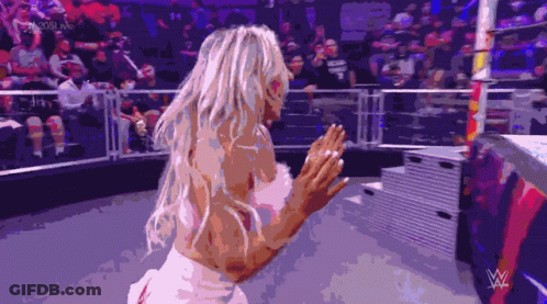 A Woman In A White Dress Is Standing In A Wrestling Ring GIF