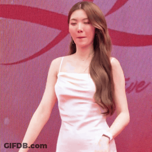 A Woman In A White Dress Is Standing In Front Of A Large Screen With The Word Love On It GIF