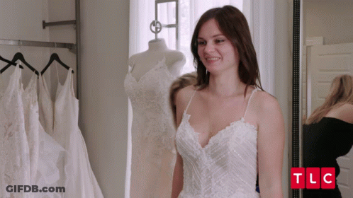 A Woman In A White Dress Is Standing In Front Of A Mirror With Tlc Written In Red Letters GIF