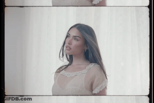 A Woman In A White Dress Is Standing In Front Of A White Curtain GIF