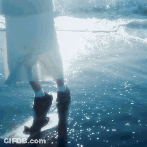 A Woman In A White Dress Is Standing In The Ocean GIF