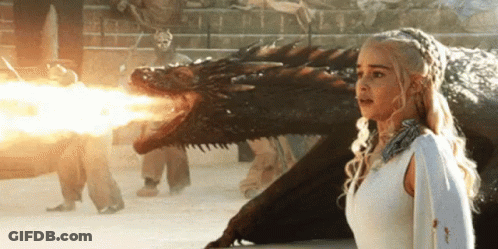 A Woman In A White Dress Is Standing Next To A Dragon That Is Shooting Fire From Its Mouth . GIF
