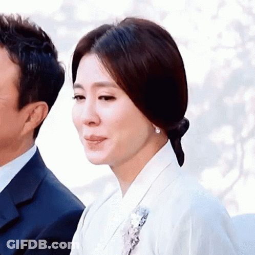 A Woman In A White Dress Is Standing Next To A Man In A Suit . GIF