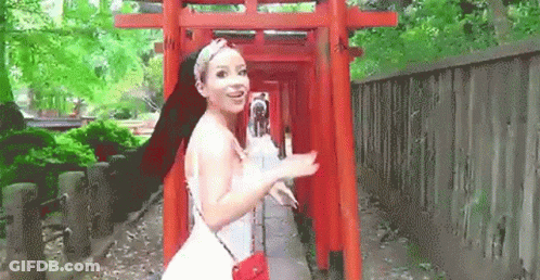 A Woman In A White Dress Is Standing Next To A Red Torii Gate . GIF