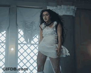 A Woman In A White Dress Is Standing Next To A Window GIF