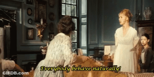 A Woman In A White Dress Is Standing Next To Another Woman In A Living Room And Saying Everybody Behave Naturally . GIF
