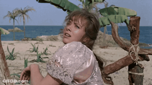 A Woman In A White Dress Is Standing On A Sandy Beach GIF