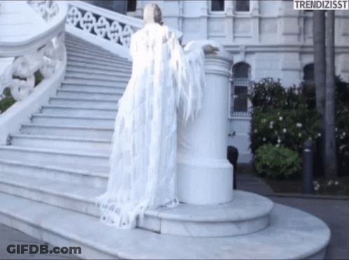 A Woman In A White Dress Is Standing On A Set Of Stairs With The Words Trendizisst On The Bottom Right GIF