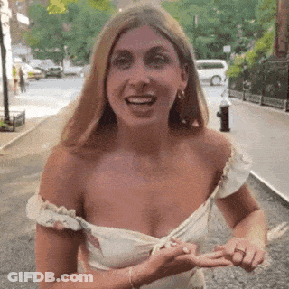 A Woman In A White Dress Is Standing On A Sidewalk . GIF