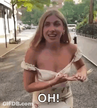 A Woman In A White Dress Is Standing On A Sidewalk With Her Breast Exposed . GIF
