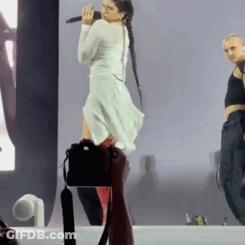 A Woman In A White Dress Is Standing On A Stage With A Microphone In Her Hand . GIF