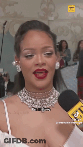 A Woman In A White Dress Is Talking Into A Microphone . GIF