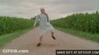 A Woman In A White Dress Is Walking Down A Dirt Road In A Field . GIF