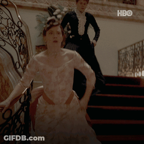 A Woman In A White Dress Is Walking Down A Set Of Stairs Next To A Woman In A Black Dress GIF
