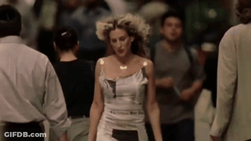 A Woman In A White Dress Is Walking In A Crowd Of People . GIF