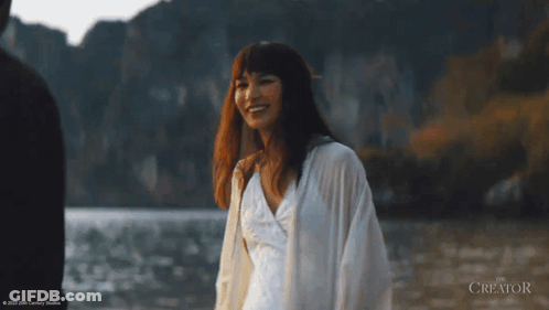 A Woman In A White Dress Is Walking In The Water With The Creator Written In The Corner GIF