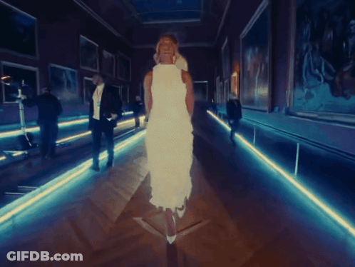 A Woman In A White Dress Is Walking Through A Dark Hallway GIF