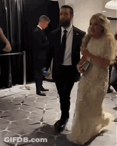 A Woman In A White Dress Is Walking With A Man In A Black Suit GIF