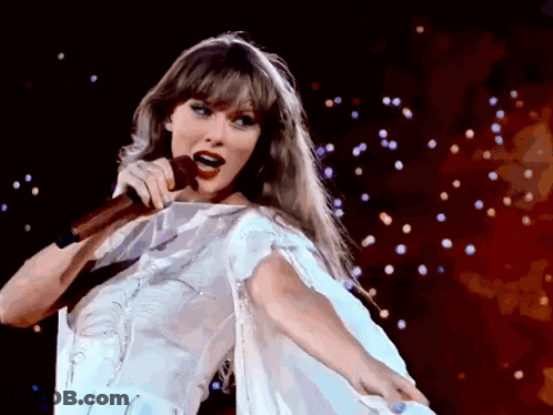 A Woman In A White Dress Singing Into A Microphone On A Stage GIF