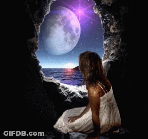 A Woman In A White Dress Sits In A Cave Looking At A Full Moon Over The Ocean GIF
