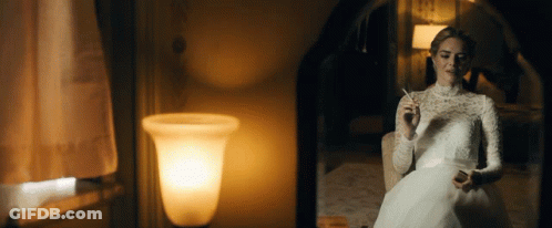 A Woman In A White Dress Smoking A Cigarette In Front Of A Mirror GIF