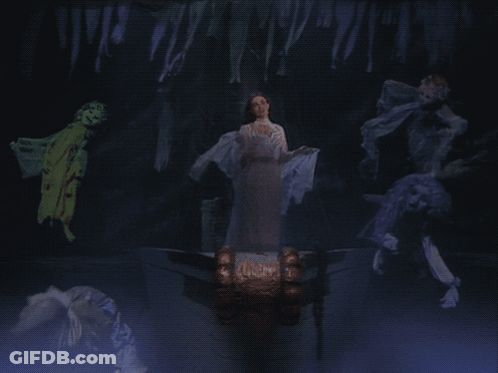A Woman In A White Dress Stands In A Dark Room Surrounded By Ghosts GIF