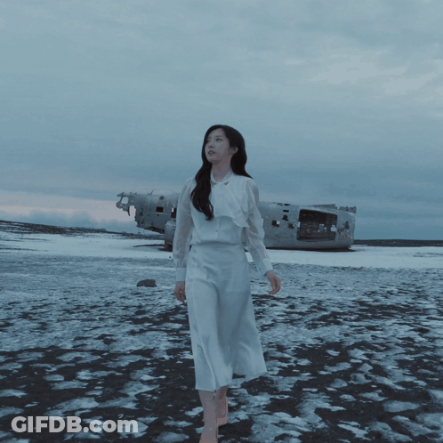 A Woman In A White Dress Stands In A Snowy Field GIF