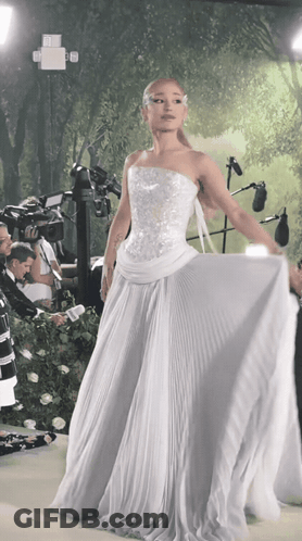 A Woman In A White Dress Stands In Front Of A Camera GIF