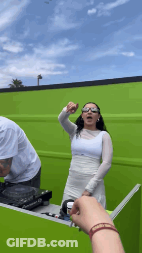 A Woman In A White Dress Stands In Front Of A Green Wall GIF