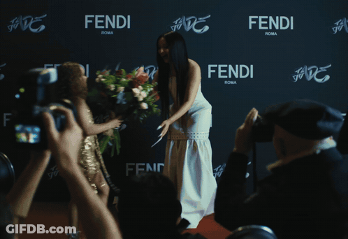A Woman In A White Dress Stands In Front Of A Wall That Says Fendi Roma GIF
