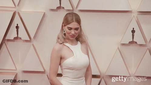 A Woman In A White Dress Stands In Front Of A Wall With Oscar Statues GIF