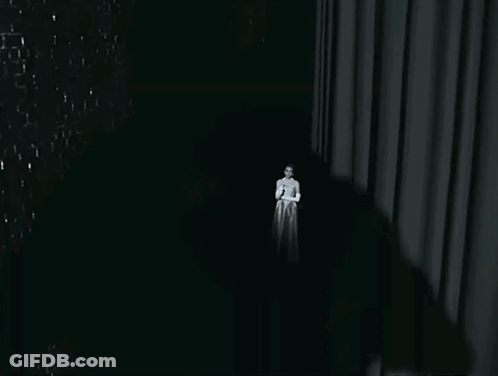 A Woman In A White Dress Stands In The Dark GIF