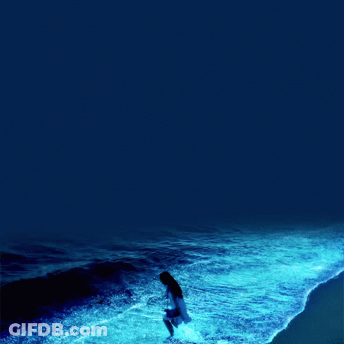 A Woman In A White Dress Stands In The Ocean GIF