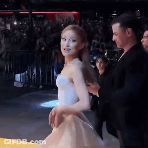 A Woman In A White Dress Walks Down A Red Carpet GIF