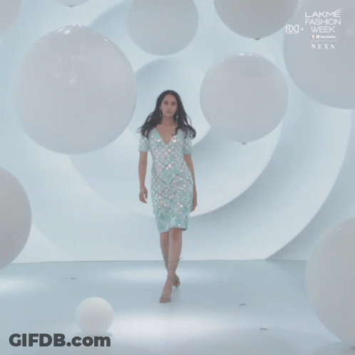 A Woman In A White Dress Walks Down A Runway At Lakme Fashion Week GIF