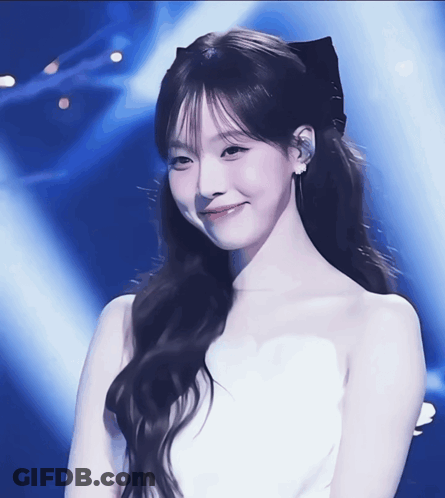 A Woman In A White Dress With A Black Bow In Her Hair Smiles GIF