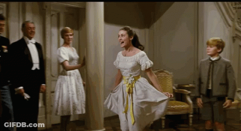 A Woman In A White Dress With A Yellow Belt Is Dancing In A Room GIF
