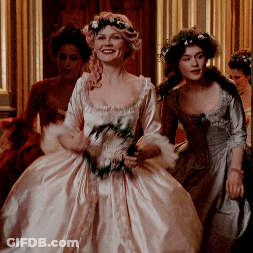 A Woman In A White Dress With Flowers In Her Hair Smiles GIF