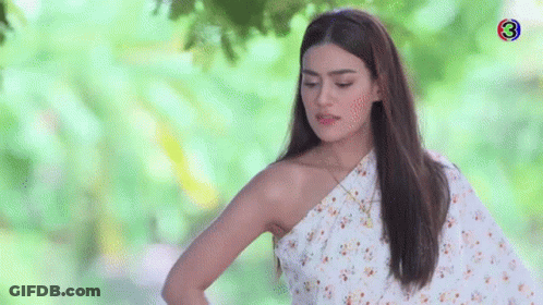 A Woman In A White Floral Dress Is Standing In Front Of A Tree . GIF