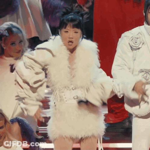 A Woman In A White Fur Coat Stands In Front Of A Red Background GIF