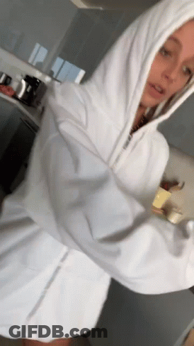 A Woman In A White Hoodie Is Standing In A Kitchen With Her Arms Outstretched . GIF