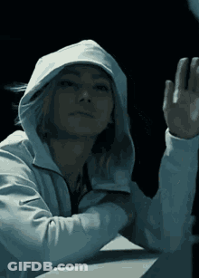 A Woman In A White Hoodie Is Waving Her Hand In The Dark GIF