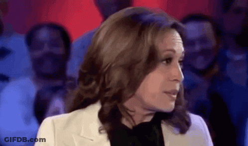 A Woman In A White Jacket And Black Shirt Is Talking To A Crowd Of People . GIF