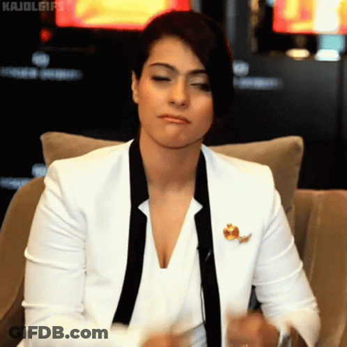 A Woman In A White Jacket And Black Tie Is Sitting On A Chair GIF