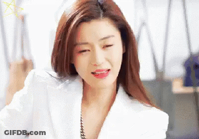 A Woman In A White Jacket And Red Lipstick Is Sitting In An Office . GIF